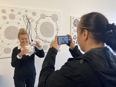 A female researcher is filming another researcher who is holding up a clear bag containing several white polystyrene balls.