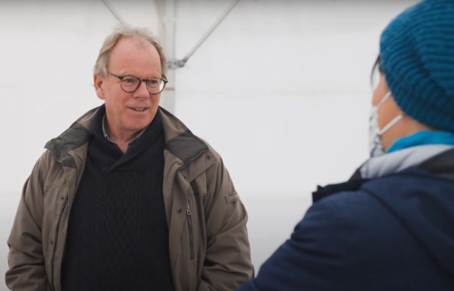 A smiling man wears a warm winter jacket inside a weather gazego 