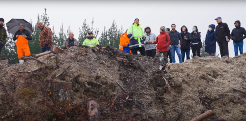 A group of 15 forestry workers and researchers look down from the top of a forestry slash hill 