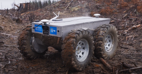 A silver rectangular box carried by four quadbike size wheels has wires and antennae on top. It is in a forestry slash setting.